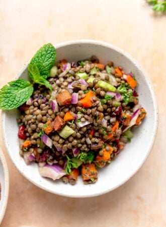 French lentil salad with fresh herbs, sweet potato and diced vegetables in a bowl garnished with fresh mint leaves.