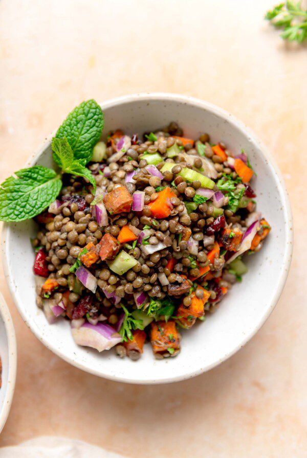 French lentil salad with fresh herbs, sweet potato and diced vegetables in a bowl garnished with fresh mint leaves.