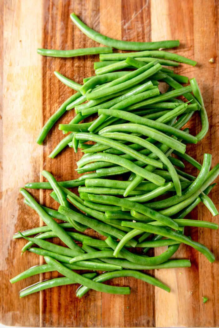A pile of washed and trimmed green beans on a wooden cutting board.