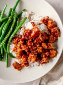 Tofu cubes tossed in a gochujang glaze over rice with a serving of green beans in a bowl.