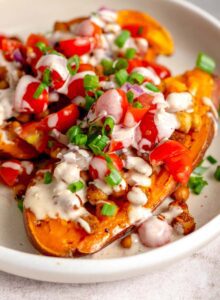 Two baked sweet potato halves topped with chickpeas, cherry tomatoes, parsley and tahini sauce.