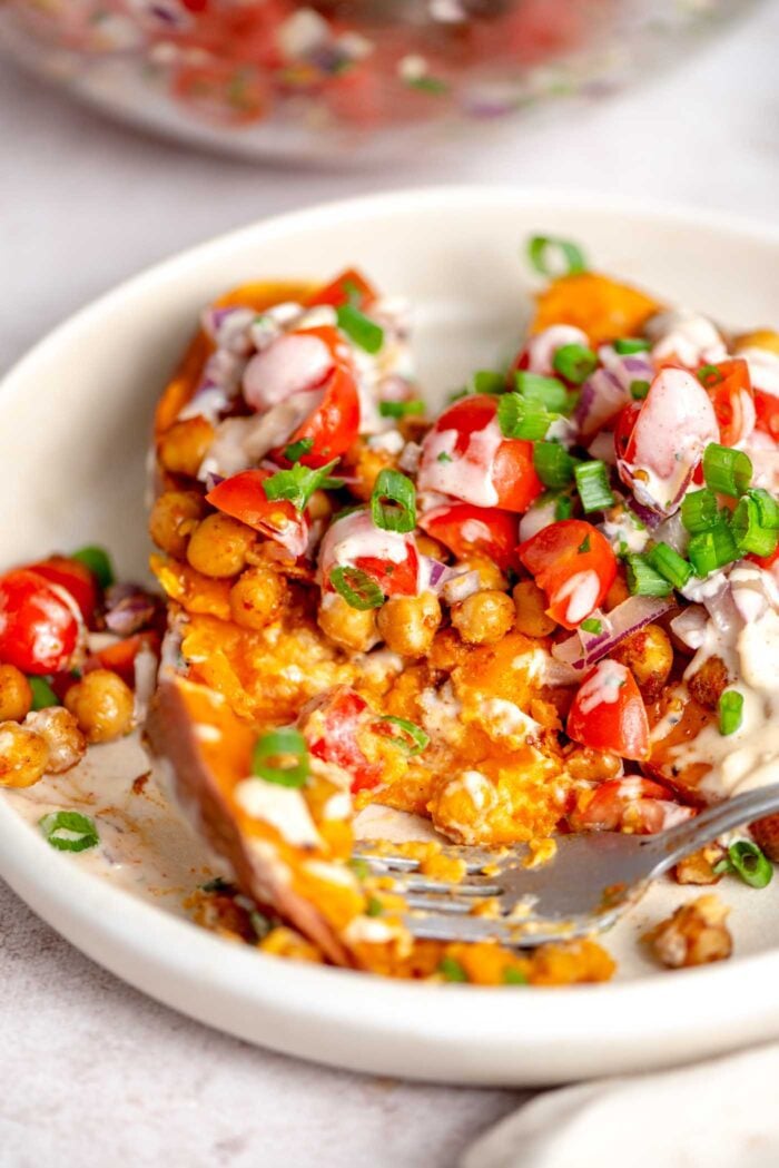 Fork on a plate of baked sweet potatoes stuffed with tomatoes, parsley and chickpeas.