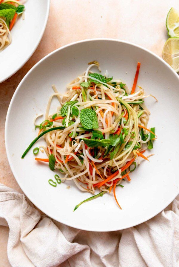 Bowl of rice noodle and vegetable salad topped with pieces of fresh herbs.