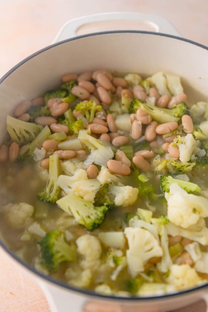 Beans, broccoli, cauliflower and potato cooking in a broth in a large pot.
