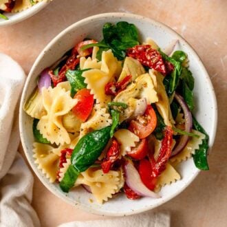 Bowl of sun dried tomato pasta salad with artichokes, spinach, red onion and tomato.