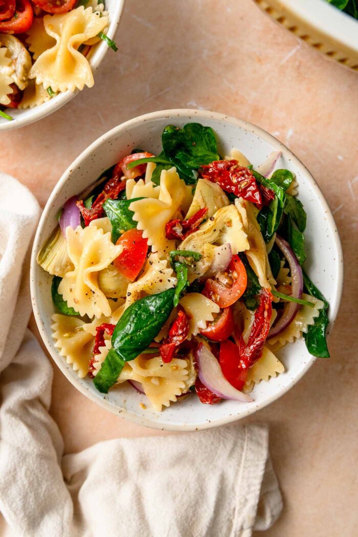 Bowl of sun dried tomato pasta salad with artichokes, spinach, red onion and tomato.