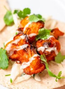 Pieces of buffalo cauliflower on a tortilla topped with cilantro and ranch sauce.