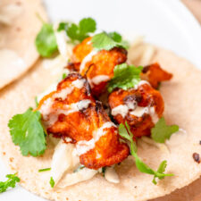 Pieces of buffalo cauliflower on a tortilla topped with cilantro and ranch sauce.