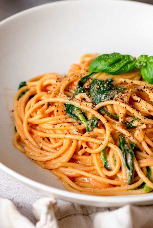 Bowl of creamy tomato pasta topped with a few leaves of fresh basil and fresh cracked black pepper.