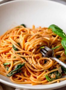 Fork in a bowl creamy tomato spaghetti topped with a few leaves of fresh basil and fresh cracked black pepper.