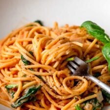 Fork in a bowl creamy tomato spaghetti topped with a few leaves of fresh basil and fresh cracked black pepper.