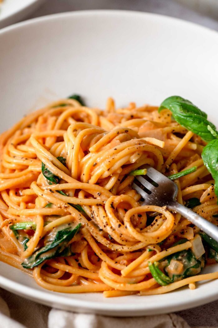 Creamy tomato spinach pasta twirled on a fork in a bowl.