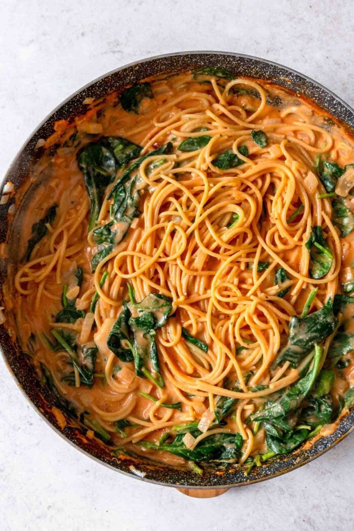 Large skillet of creamy tomato spaghetti with spinach.