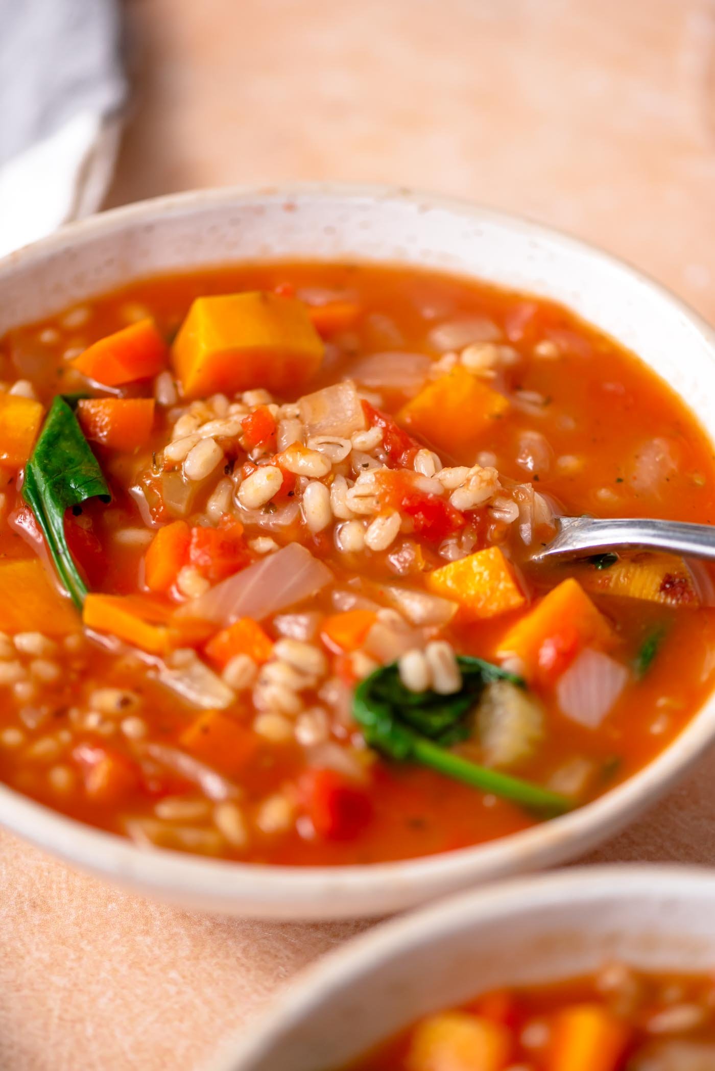 Spoon in a bowl of vegetable barley soup with sweet potato and spinach.