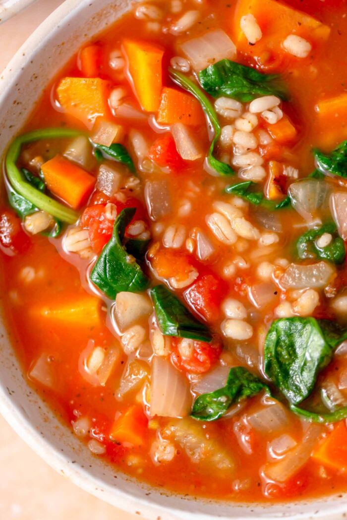 Bowl of vegetable barley soup with spinach, sweet potato, carrot and onion.