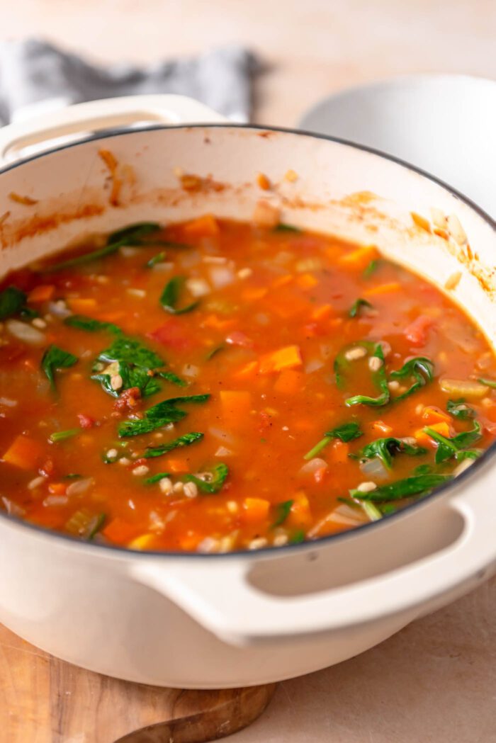 Tomato barley vegetable soup with spinach cooking in a large pot.