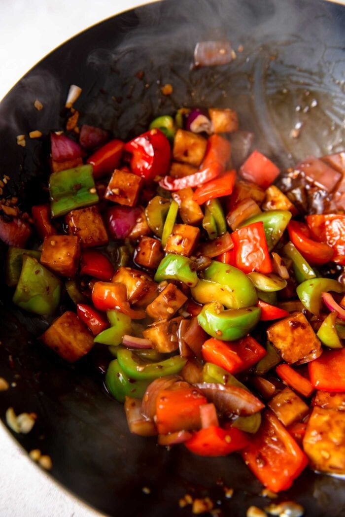 Cubes of tofu, bell pepper and onion cooking in a sauce in a wok.