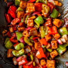 Tofu cubes with chopped pepper and onions in sauce in a wok.