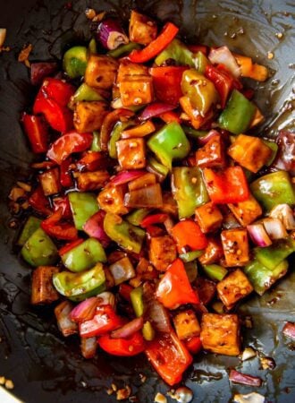 Tofu cubes with chopped pepper and onions in sauce in a wok.