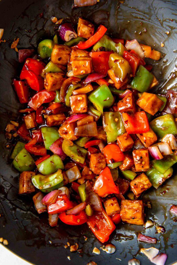 Tofu cubes with chopped pepper and onions in sauce in a wok.