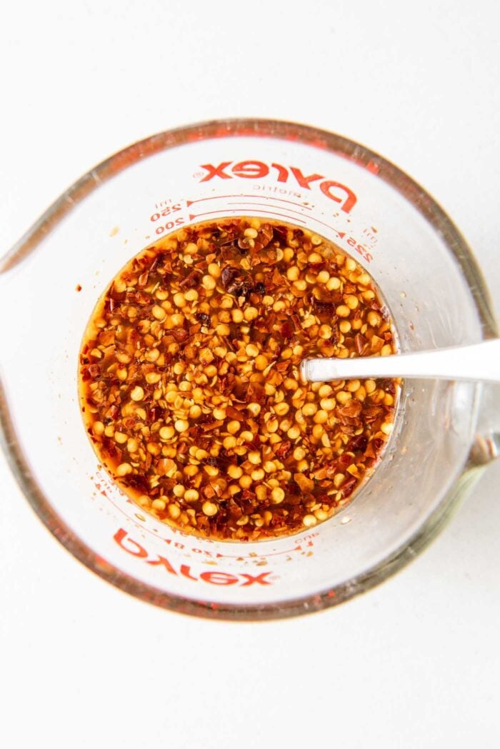 Sauce with red pepper flakes in it in a measuring cup with a spoon in it.