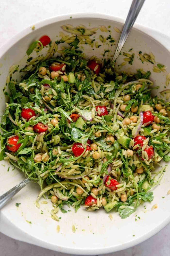 Orzo pesto salad with tomatoes and chickpeas in a large mixing bowl.