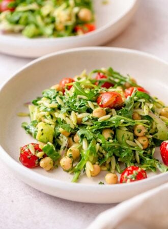 Plate of orzo pesto salad with tomatoes, arugula, red onion and chickpeas.