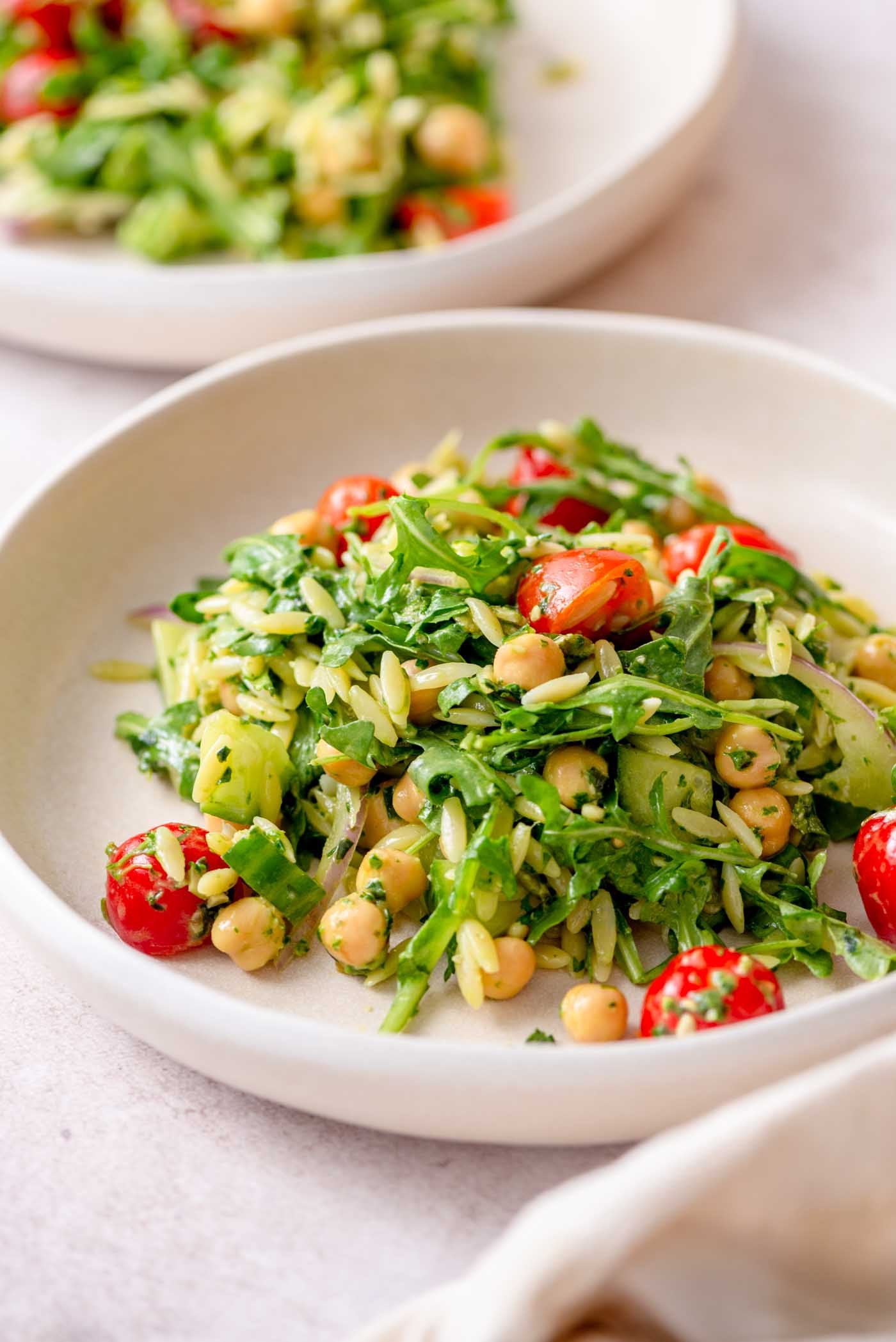 Plate of orzo pesto salad with tomatoes, arugula, red onion and chickpeas.