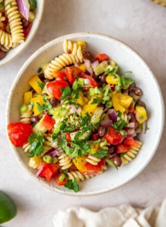 Bowl of black bean pasta salad with tomatoes, cucumber, cilantro and corn.