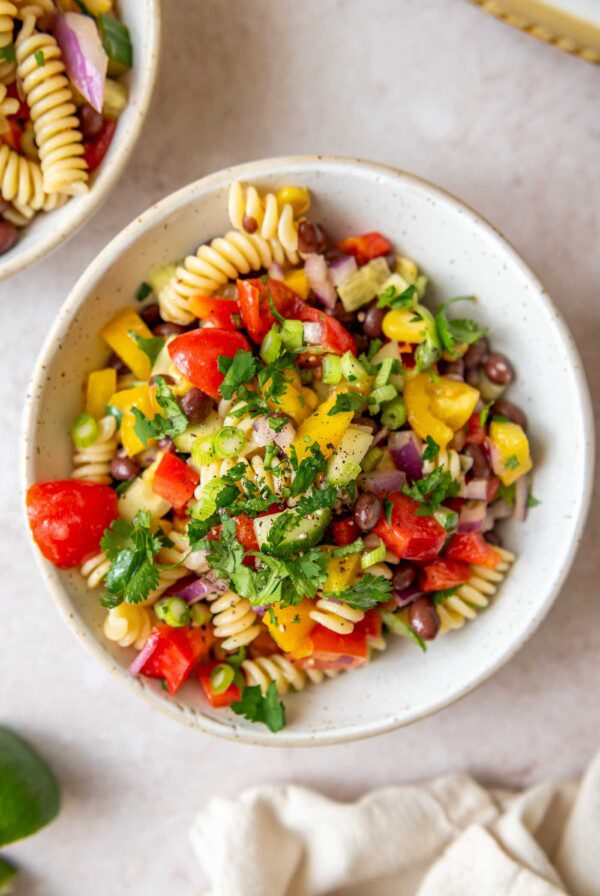 Bowl of black bean pasta salad with tomatoes, cucumber, cilantro and corn.