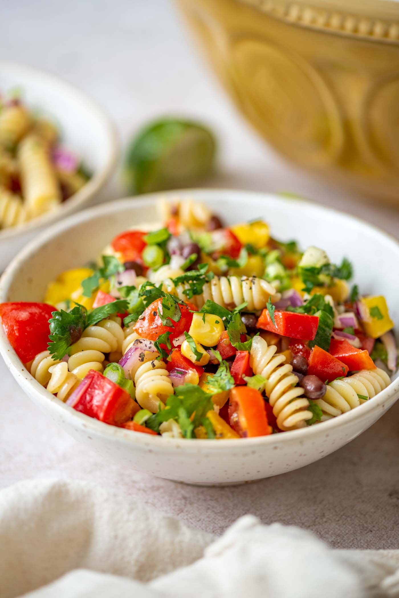 Bowl of black bean pasta salad with tomatoes, cucumber, cilantro and corn.