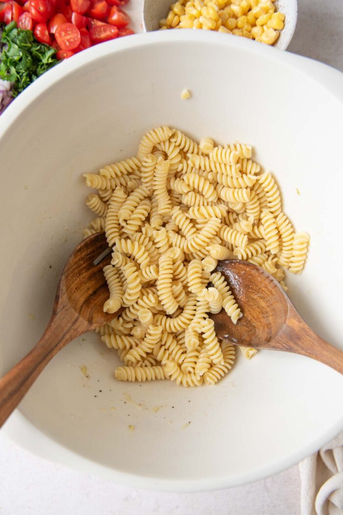 Cooked pasta in a large mixing bowl with two wooden salad spoons in it.
