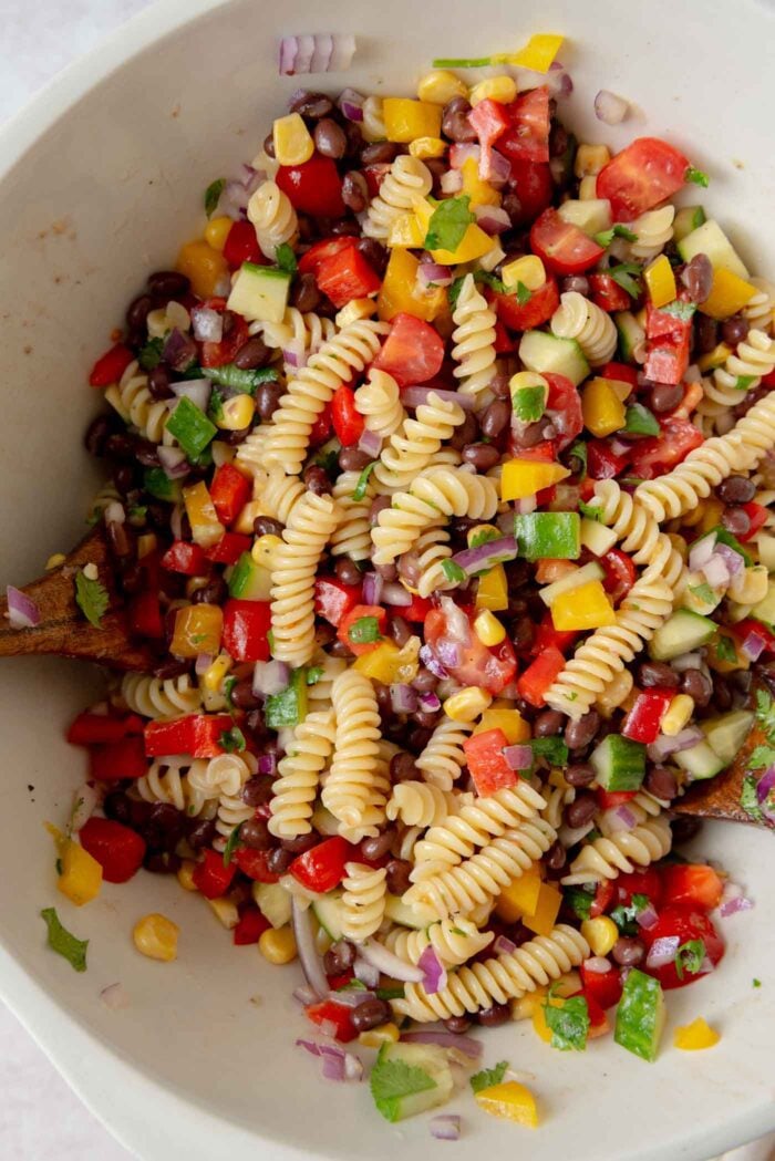Large mixing bowl of a black bean pasta salad with corn, cucumber and bell peppers.
