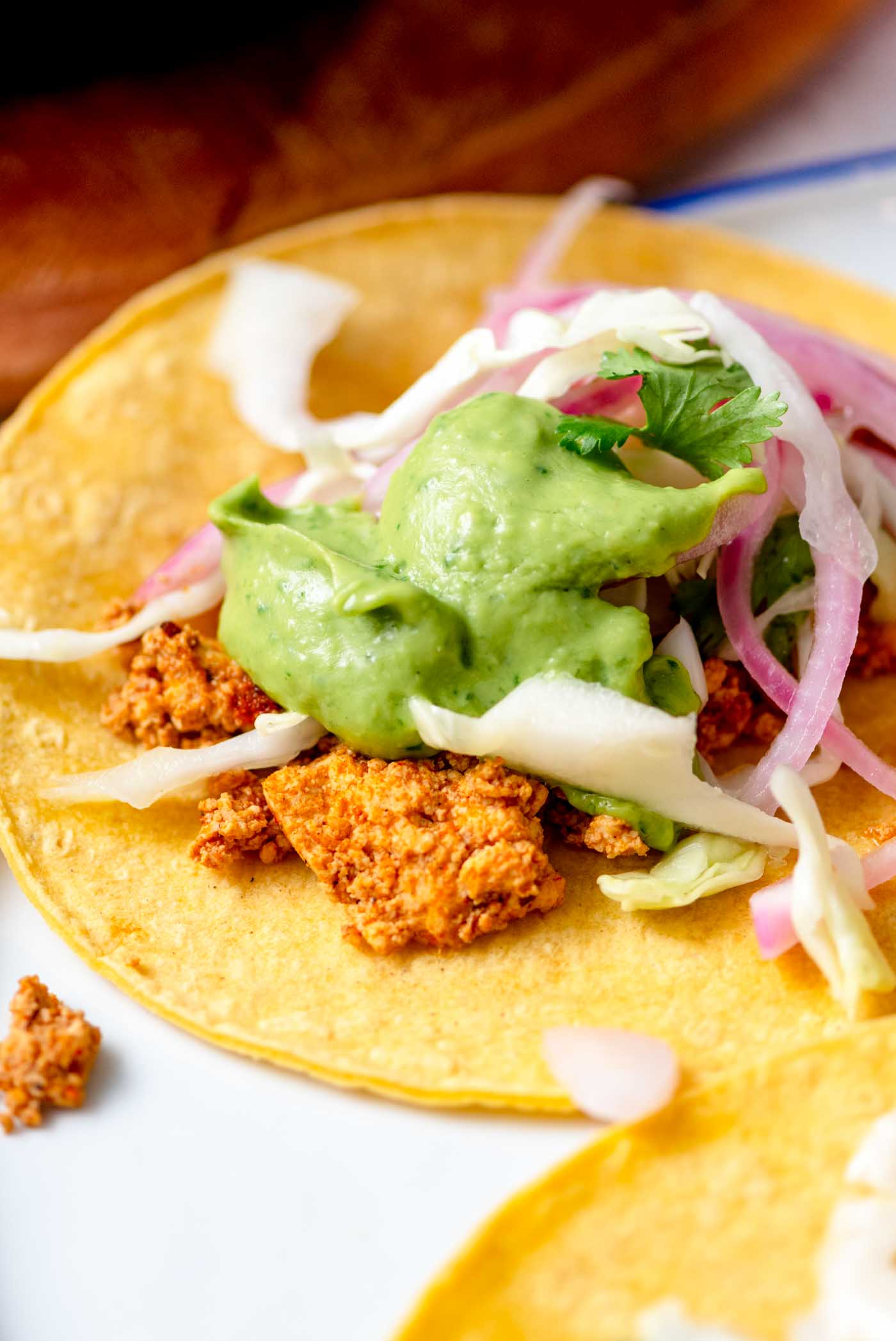 A single, perfectly assembled tofu taco, adorned with creamy avocado sauce, bright pickled onion, and crisp cabbage, showcasing its delicious layers.