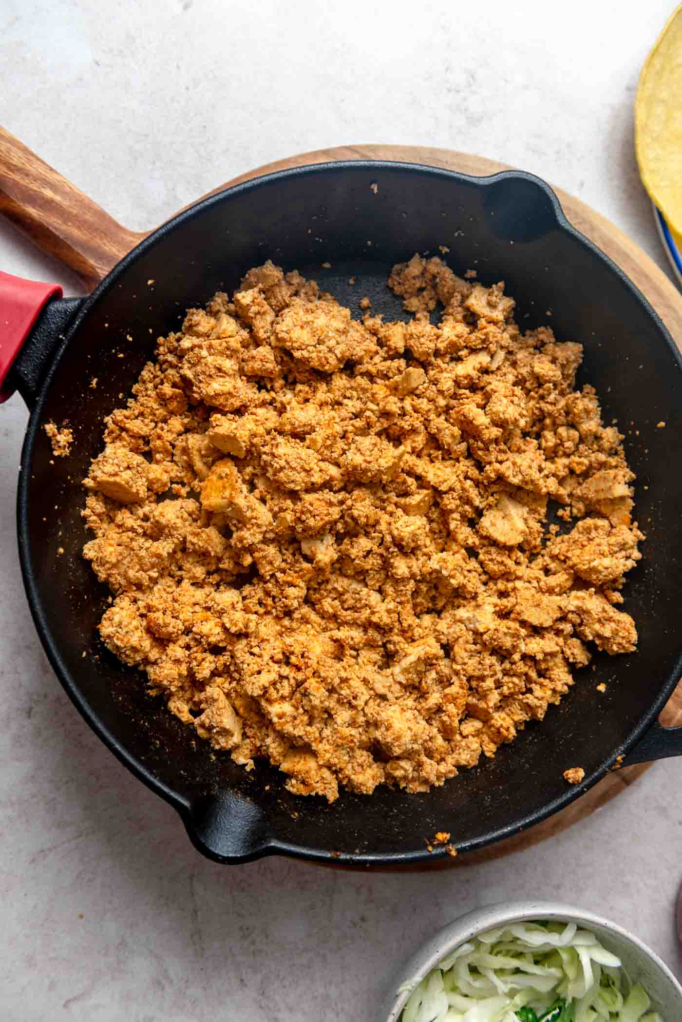 Seasoned tofu crumbles sizzling and browning in a cast iron skillet, absorbing the rich flavors of the spices.