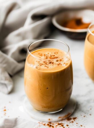 A creamy sweet potato smoothie in a glass sprinkled with cinnamon with a dish cloth laid out behind it.
