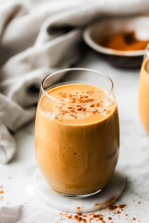 A creamy sweet potato smoothie in a glass sprinkled with cinnamon with a dish cloth laid out behind it.