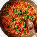 Large pan of tomato orzo with spinach with a wooden spoon resting in pan.