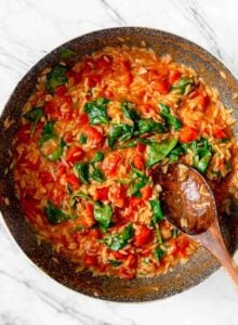 Large pan of tomato orzo with spinach with a wooden spoon resting in pan.
