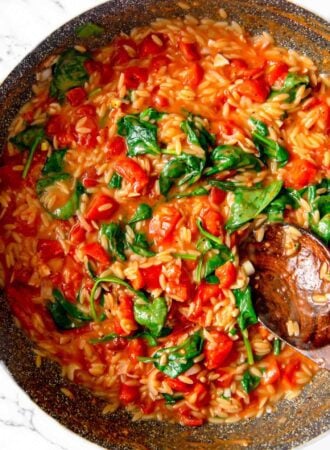 Tomato orzo with spinach cooking in a pan with a spoon resting in it.