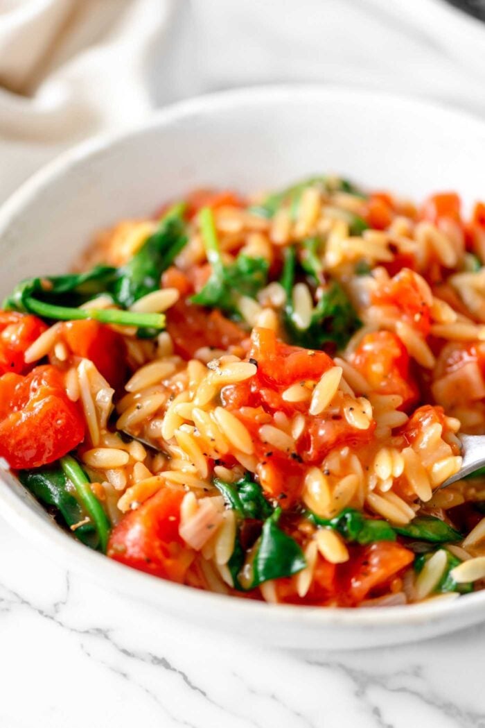 Fork in a bowl of tomato orzo with spinach.