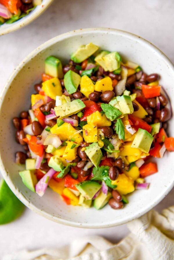 Bowl of mango and black bean salad with avocado, red bell pepper, red onion and cilantro.