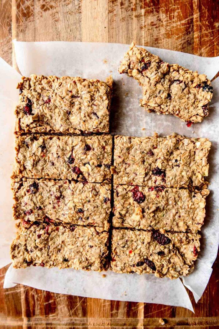 Cranberry granola bars cut into 8 bars on a cutting board with one bar off to the side with a bite taken out of it.