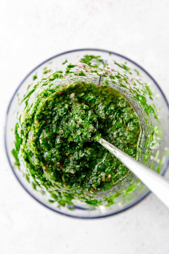 Chimmichurri sauce in a food processor with a spoon sitting in it.