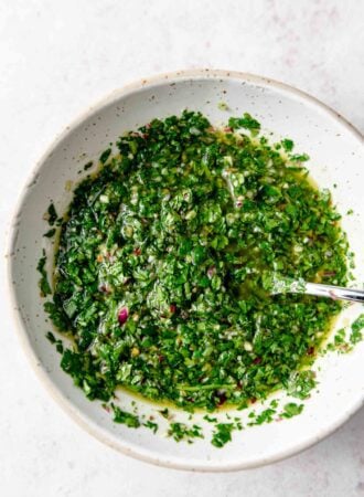 Vibrant green chimmichurri sauce in a bowl with a spoon.