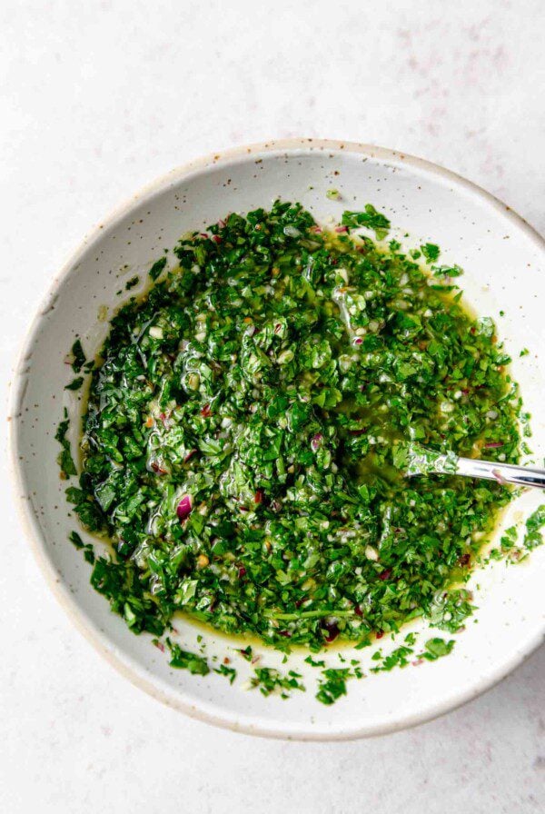 Vibrant green chimmichurri sauce in a bowl with a spoon.