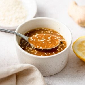 Spoon lifting some sesame miso ginger dressing from a small bowl. The dressing has sesame seeds in it.