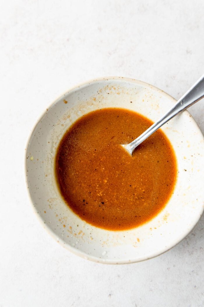 Bowl of miso sesame salad dressing with bits of garlic and black pepper.