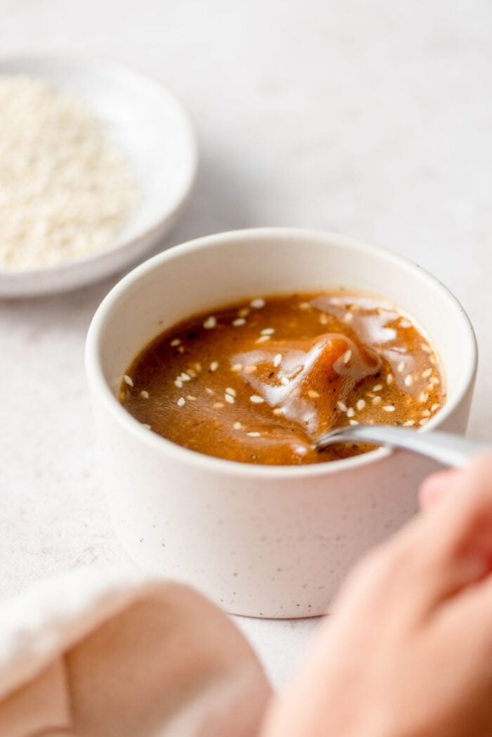 Using a spoon to stir a dish of sesame seed ginger miso dressing.