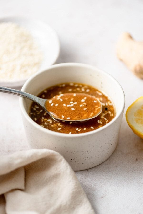 Spoon lifting some sesame miso ginger dressing from a small bowl. The dressing has sesame seeds in it.